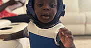 Muhammad joined the competition — help win amazing prizes! toddler, child, helmet, protective_vest, indoor, living_room, couch, carpet, furniture, curious, reaching, person, clothing, short_sleeves, plaid_shirt, black_skin, young_child, home, blurred_background, soft_lighting