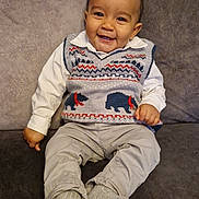Malachi joined the competition — help win amazing prizes! baby, child, smiling, sweater_vest, bear_pattern, couch, socks, pants, white_shirt, curly_hair, indoor, portrait, happy, seated, cute, young_child, fabric, cozy, home, person