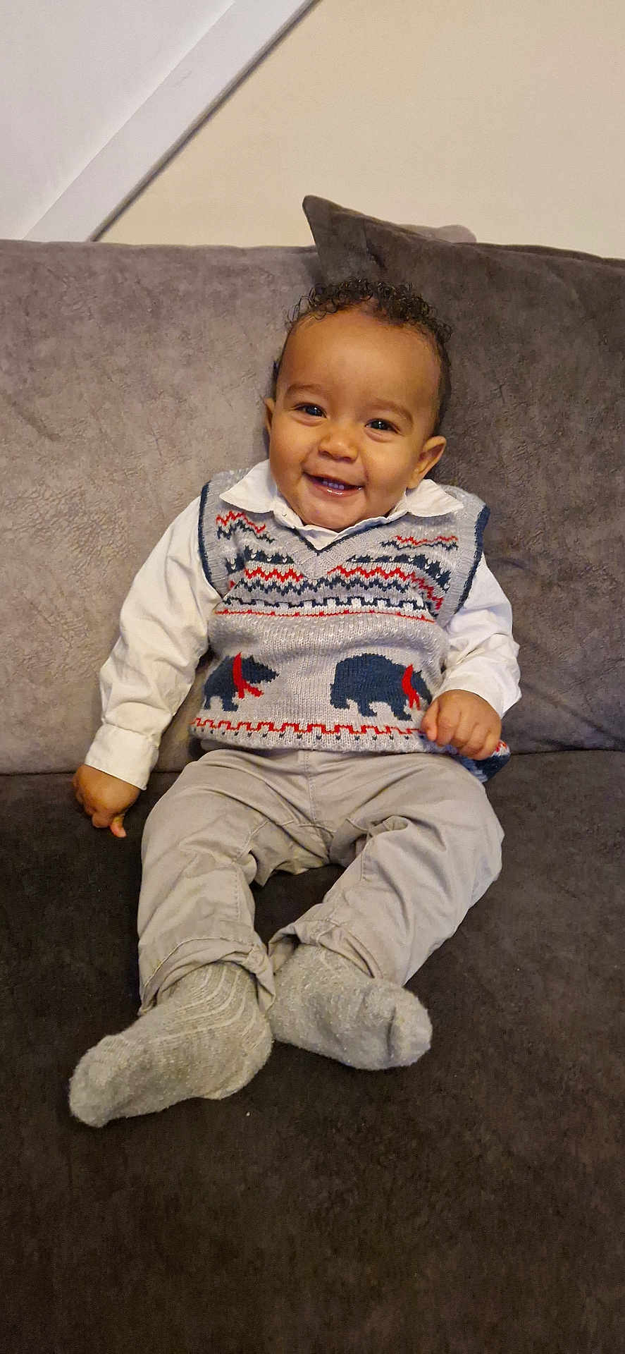 Malachi joined the competition — help win amazing prizes! baby, child, smiling, sweater_vest, bear_pattern, couch, socks, pants, white_shirt, curly_hair, indoor, portrait, happy, seated, cute, young_child, fabric, cozy, home, person