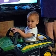 Legacy is registered to the contest to win money with this photo: child, toddler, toy_car, john_deere, indoor, person, adult, shorts, purple_shirt, television, gaming_controller, furniture, carpet, hands, face, curious, vehicle, play, home, standing
