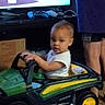 child, toddler, toy_car, john_deere, indoor, person, adult, shorts, purple_shirt, television, gaming_controller, furniture, carpet, hands, face, curious, vehicle, play, home, standing