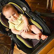 Brantley is registered to the contest to win money with this photo: baby, child, infant, smiling, portrait, car_seat, stroller, seated, indoors, wooden_floor, yellow_shirt, barefoot, toes, happy, looking_at_camera, close_up, baby_gear, warm_lighting, home, person