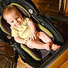 baby, child, infant, smiling, portrait, car_seat, stroller, seated, indoors, wooden_floor, yellow_shirt, barefoot, toes, happy, looking_at_camera, close_up, baby_gear, warm_lighting, home, person
