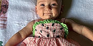 Addison is registered to the contest to win money with this photo: baby, infant, child, smiling, dress, headband, flower, blanket, patterned_clothing, pink, green, laying_down, cute, happy, indoor, portrait, face, skin, young, person