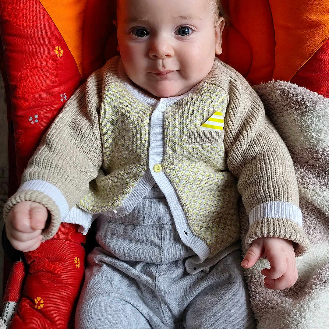 Gabriel participe au concours pour gagner de l'argent avec cette photo : baby, blanket, casual, child, comfortable, cozy, cute, face, hands, indoor, infant, knitwear, legs, orange_cushion, portrait, seated, smiling, soft_texture, warm_clothing, young