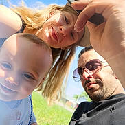 Zachery is registered to the contest to win money with this photo: baby, woman, man, smile, outdoor, sunlight, grass, sunglasses, portrait, family, happy, blue_sky, casual_clothing, short_hair, long_hair, headwear, selfie, face, person, nature