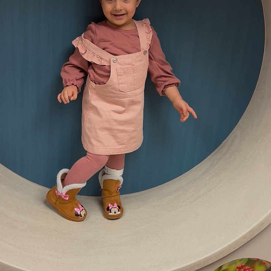 Marcellina is registered to the contest to win money with this photo: boots, child, circular_frame, clothing, cute, fashion, feet, floor, girl, happy, indoor, minnie_mouse, pink_dress, playful, portrait, pose, smile, standing, wall, young_child