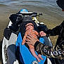 Kynoah is registered to the contest to win money with this photo: baby, infant, jet_ski, water, hand, person, orange_clothing, hat, outdoor, beach, shore, calm, watercraft, blue, white, ripples, sunlight, adult_hand, holding_hand, relaxation