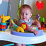 activity_center, baby, child, clothing, colorful, cute, engaged, floor, furniture, giraffe_toy, home, indoor, infant, lion_toy, person, play, red_butterfly_toy, smiling, toys, wooden_floor