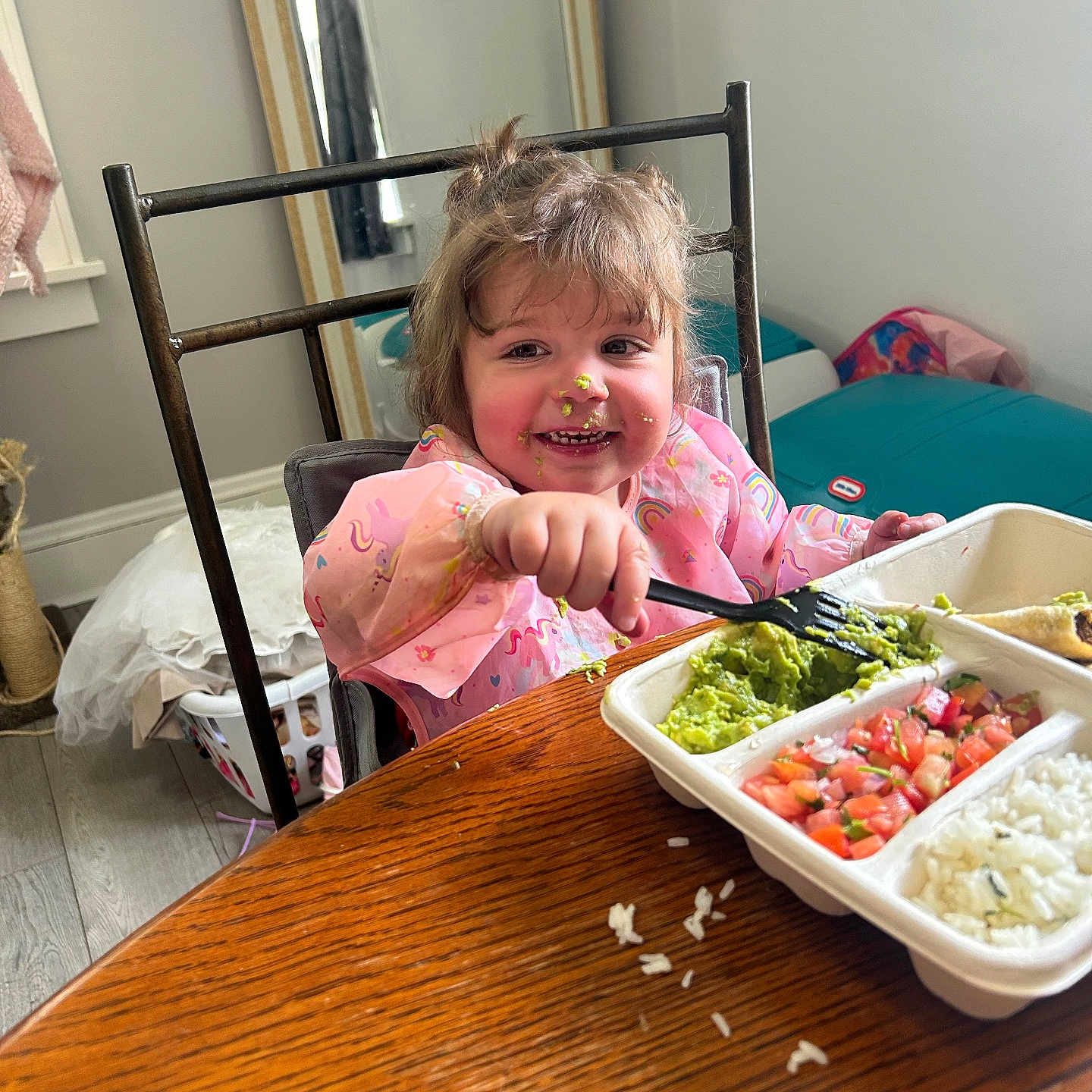 Gabriella is registered to the contest to win money with this photo: child, toddler, food, meal, fork, table, wood, messy, face, pink_clothing, high_chair, indoor, mirror, laundry_basket, rice, guacamole, tomato_salad, happy, smile, eating