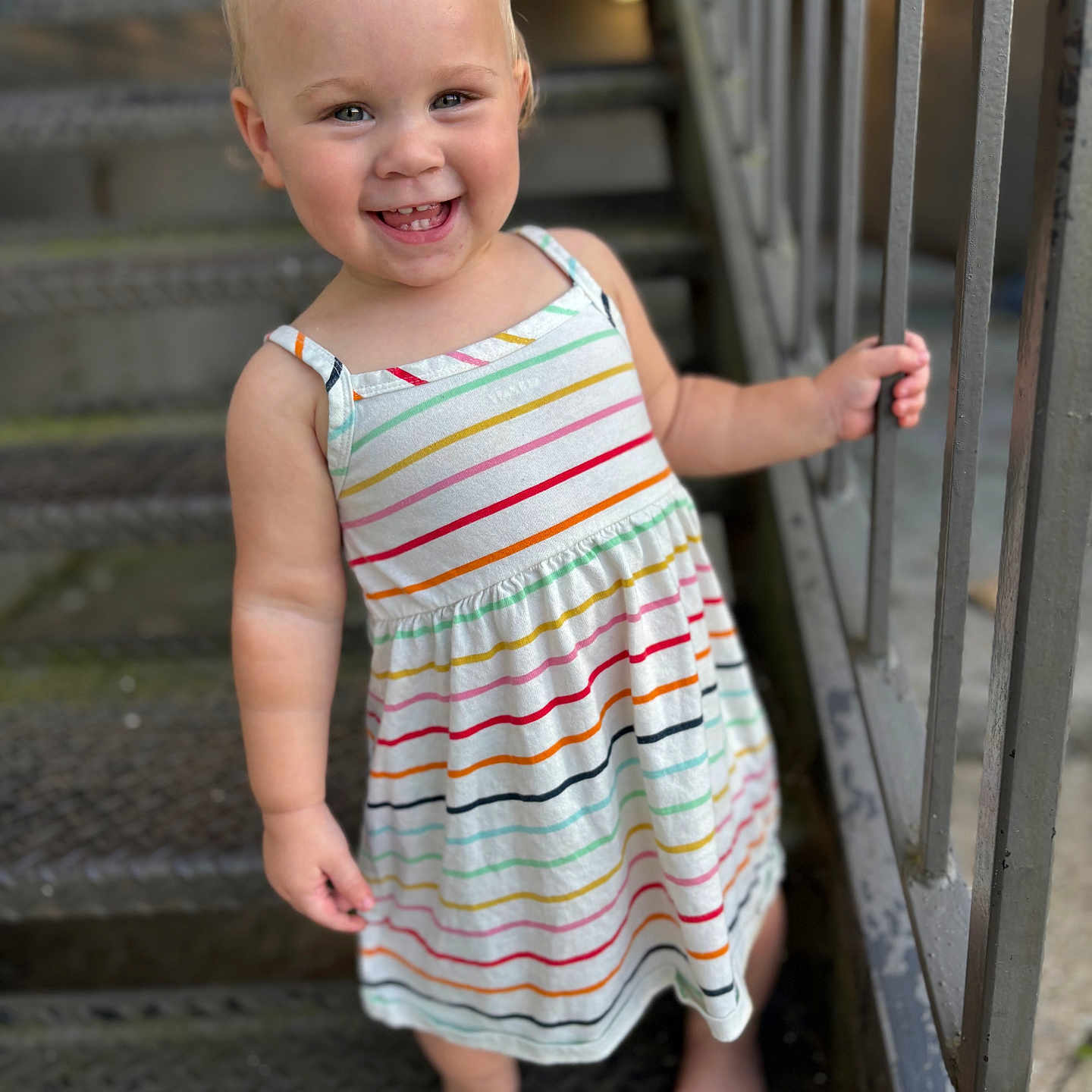 Elisia is registered to the contest to win money with this photo: barefoot, child, cute, daylight, feet, hair, happy, holding, metal_stairs, outdoor, person, portrait, railing, skin, smiling, standing, striped_dress, summer_clothing, toddler, young_child