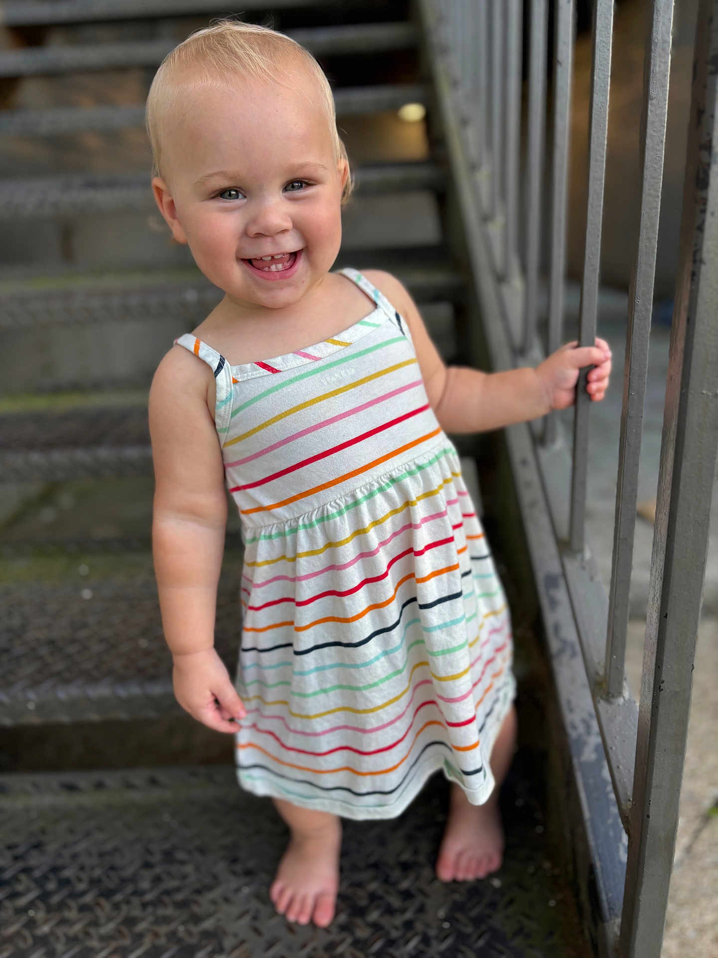 Elisia is registered to the contest to win money with this photo: toddler, child, smiling, barefoot, striped_dress, metal_stairs, railing, outdoor, happy, person, portrait, young_child, cute, standing, summer_clothing, daylight, skin, hair, feet, holding