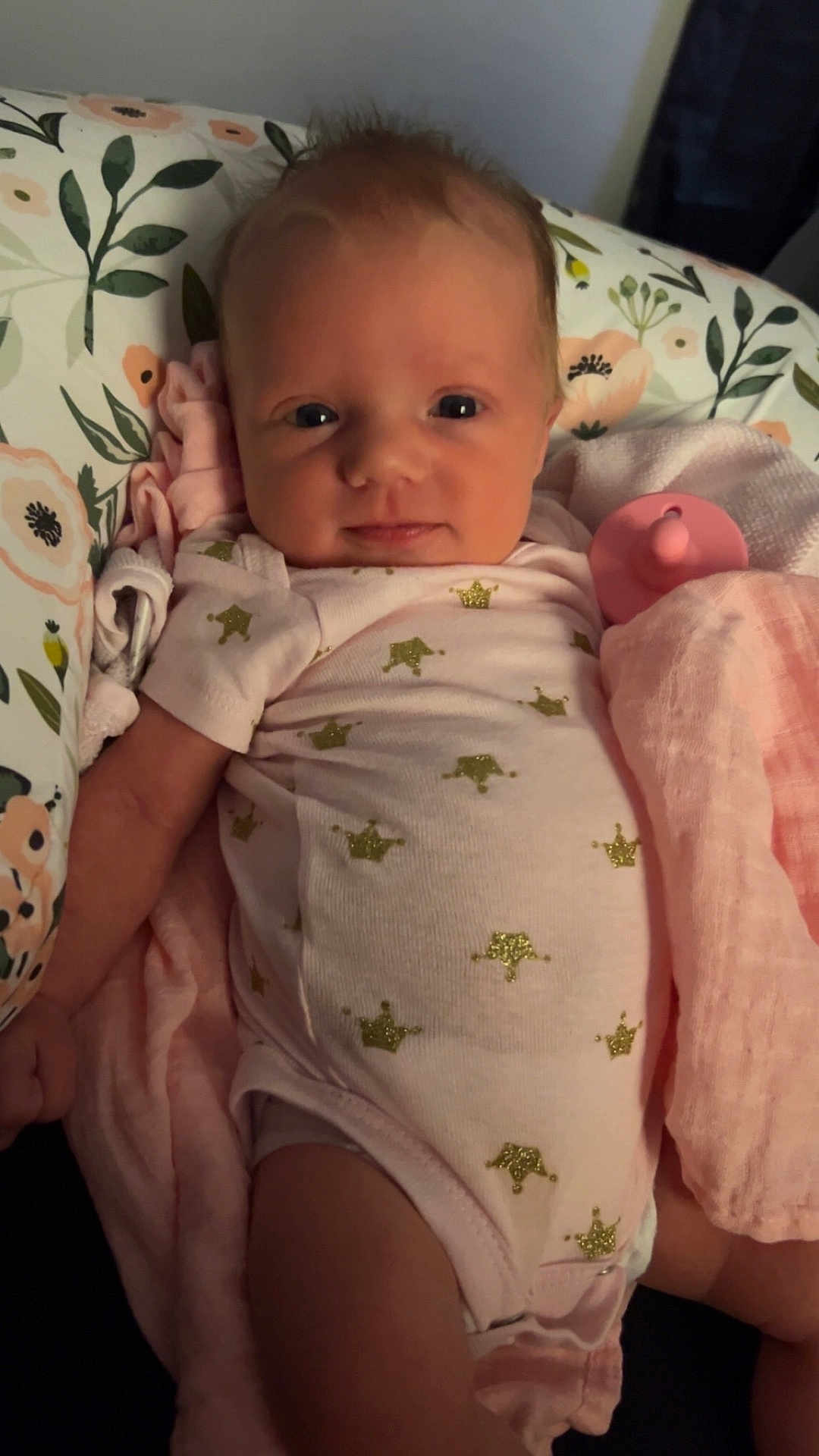 Reagan is registered to the contest to win money with this photo: baby, infant, blanket, pacifier, onesie, crown_pattern, pink, white_clothing, face, skin, hand, arm, indoor, soft_lighting, newborn, cute, lying_down, fabric, child, portrait