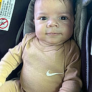 Brian is registered to the contest to win money with this photo: baby, infant, child, car_seat, clothing, nike_logo, cute, smile, face, person, indoors, seatbelt, safety, portrait, young_child, head, hand, apparel, sitting, seat