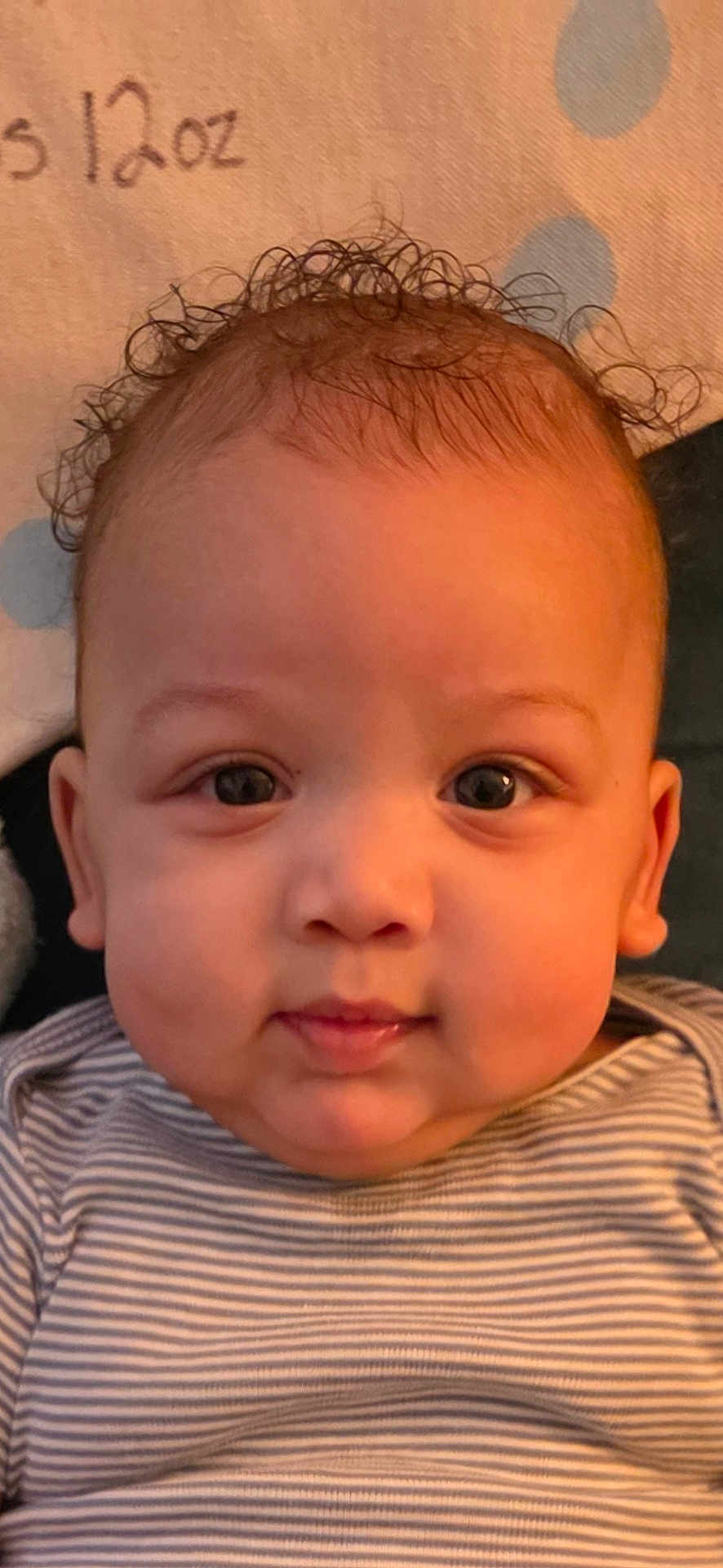Logan is registered to the contest to win money with this photo: baby, infant, face, curly_hair, striped_shirt, close_up, child, portrait, cute, looking_at_camera, indoor, skin, young_child, head, expression, person, young_baby, cheeks, eyes, soft_background