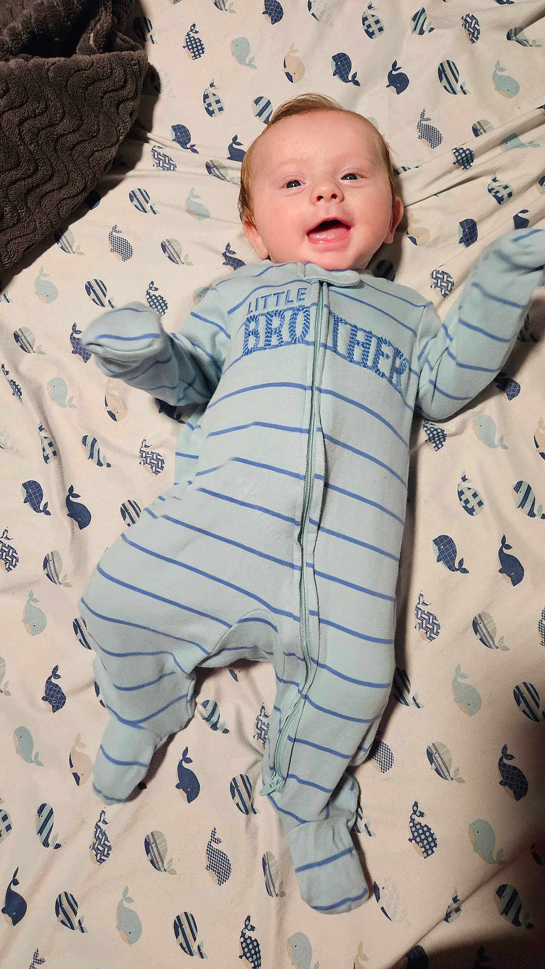 Michael is registered to the contest to win money with this photo: baby, infant, smiling, onesie, striped_clothing, blue_clothing, blanket, whale_pattern, happy, lying_down, face, arm_movement, footed_pajamas, cute, child, cheerful, indoor, soft_texture, fabric, sleepwear