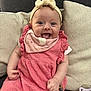 baby, bow, child, clothing, couch, cushion, cute, face, hand, happy, headband, indoor, infant, pacifier, person, pink_dress, playful, sitting, smiling, tongue_out