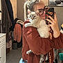 woman, cat, mirror, selfie, glasses, bathroom, coat, portrait, indoor, casual, jeans, long_hair, light, sink, phone, decor, framed_picture, tile_floor, hand, pet