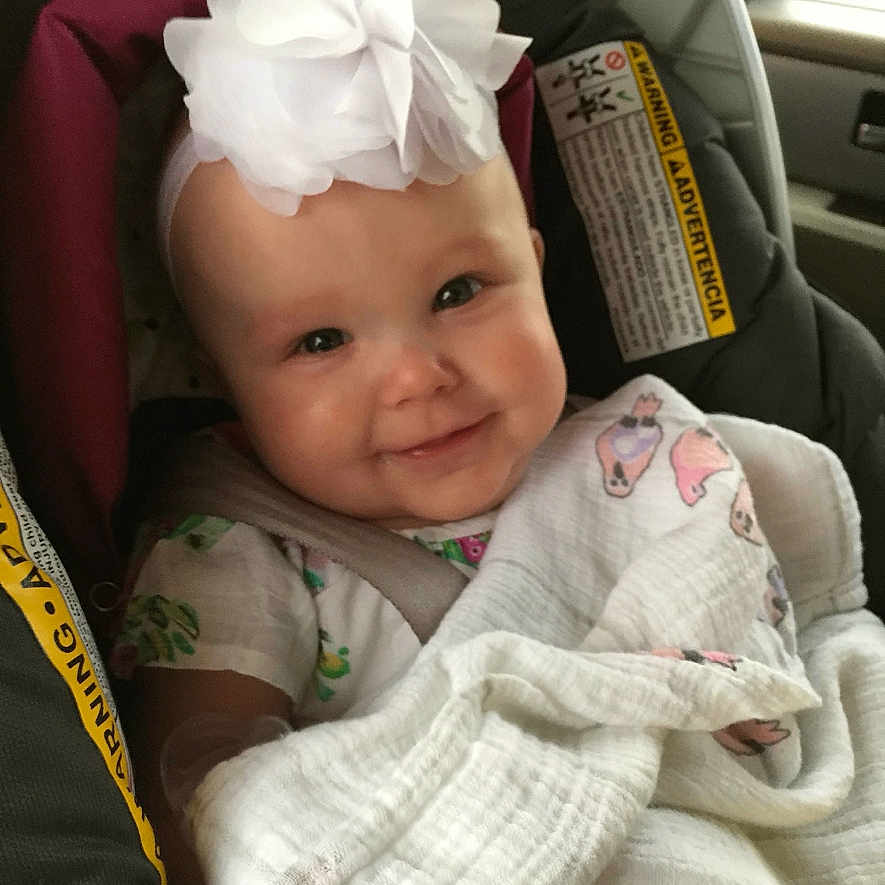 Ava joined the competition — help win amazing prizes! baby, car_seat, blanket, headband, smile, infant, child, seatbelt, cute, indoors, car, clothing, white_flower, happy, portrait, baby_girl, soft_lighting, comfortable, wrapped, seat