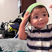 Charley joined the competition — help win amazing prizes! toddler, child, indoor, clothing, striped_shirt, green_beanie, face, smiling, hand, motion_blur, wardrobe, pile_of_clothes, blanket, bed, person, cute, expression, home, casual, portrait