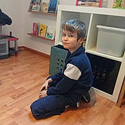 Aaron participe au concours pour gagner de l'argent avec cette photo : blue_jacket, bookshelf, boy, casual_clothing, child, floor, home, indoor, kid, leisure, playroom, short_hair, sitting, smile, sneaky, storage, toy, toy_blocks, wooden_floor, young