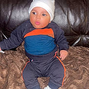 Loann a rejoint le concours — aidez-le/la à gagner de superbes lots ! baby, child, infant, sitting, blanket, leather_couch, white_hat, white_shoes, sportswear, curious, indoor, cozy, cute, small_hands, wide_eyes, puckered_lips, dark_background, soft_texture, comfortable, portrait