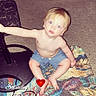 toddler, child, carpet, rug, laundry_basket, clean_clothes, indoor, floor, shorts, bare_chest, blurry, standing_lamp, cord, colorful, patterned, hand, reaching, heart_emoji, timestamp, home