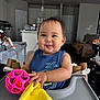 baby, infant, high_chair, toy, yellow_cloth, smile, face, kitchen, indoor, child, person, furniture, play, cute, expression, clothing, home, living_room, happy, seat