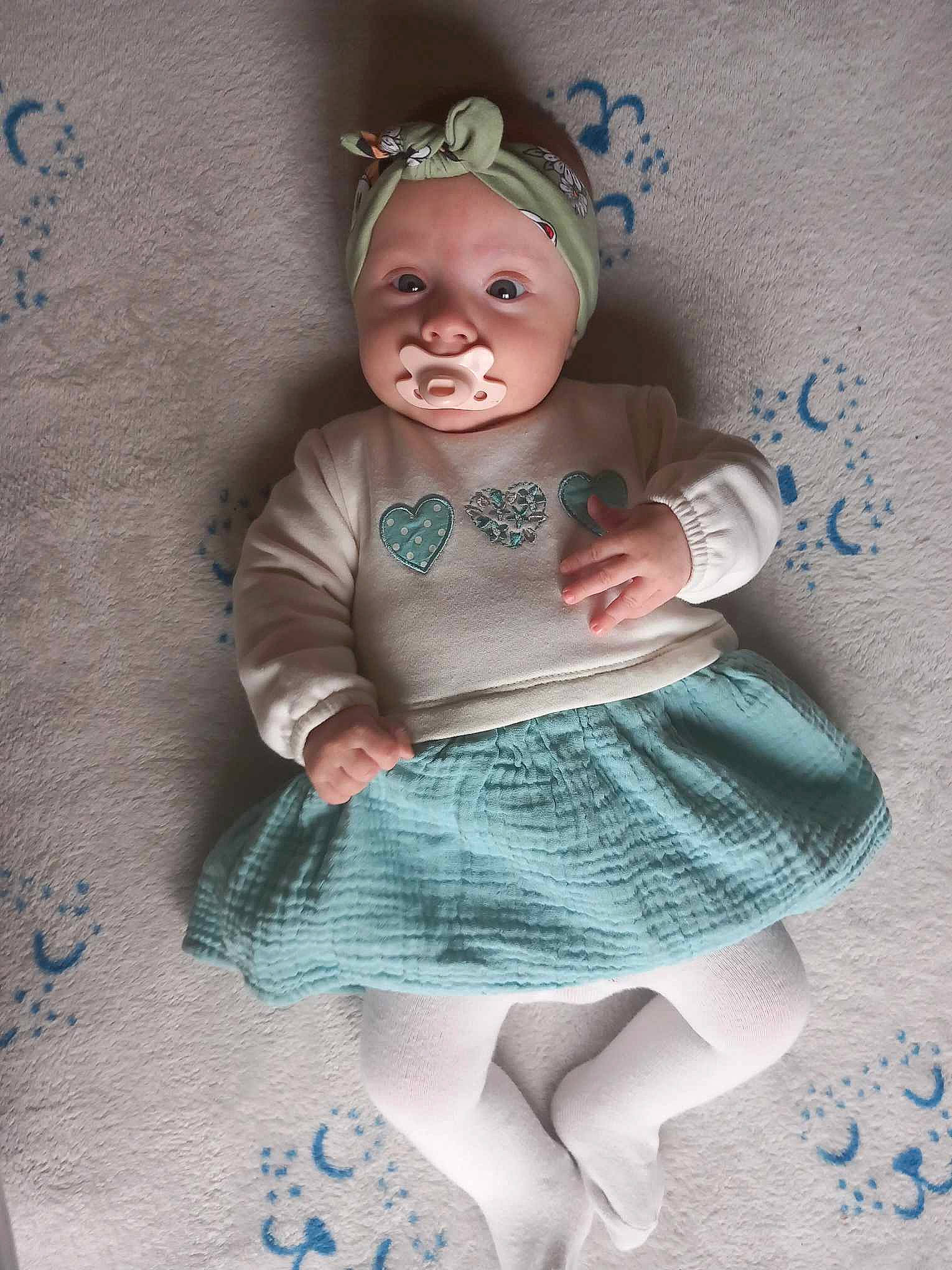 Tessa participe au concours pour gagner de l'argent avec cette photo : baby, baby_products, baby_toddler_clothing, child, eyelash, fashion_accessory, grey, hair_accessory, headband, headpiece, headwear, jewellery, linens, pattern, person, pink, sitting, sleeve, sock, textile