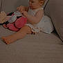 toddler, child, plush_toy, couch, indoor, cute, focused, sitting, white_dress, hair_ties, toy, soft_lighting, home, cozy, small_person, infant, playful, face, barefoot, candid