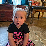 Lana is registered to the contest to win money with this photo: toddler, child, sitting, pigtails, floor, tile, black_shirt, patterned_pants, indoor, wooden_chest, chair, pillow, pumpkin_patch, curious, hands, face, person, home, furniture, casual