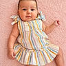 Sophia Green is registered to the contest to win money with this photo: arms, baby, child, colorful_clothing, cute, eyes, face, happy, indoors, infant, legs, lying_down, person, pink_background, portrait, ruffled_sleeves, skin, smiling, soft_texture, striped_dress