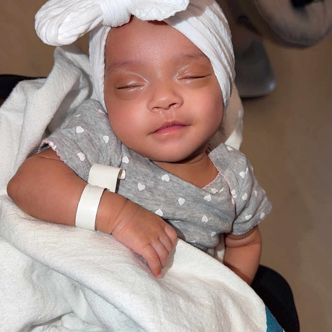 Kali is registered to the contest to win money with this photo: baby, infant, sleeping, blanket, headwrap, bow, grey_clothing, heart_pattern, nursery, hospital_band, peaceful, cute, child, soft_lighting, indoors, newborn, person, resting, wrapped, adorable