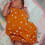 Ariya is registered to the contest to win money with this photo: newborn, baby, sleeping, orange_dress, patterned_clothing, crib, bedding, pillow, blanket, infant, peaceful, cute, sleep, indoors, soft_lighting, resting, child, tiny, cozy, portrait