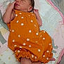 newborn, baby, sleeping, orange_dress, patterned_clothing, crib, bedding, pillow, blanket, infant, peaceful, cute, sleep, indoors, soft_lighting, resting, child, tiny, cozy, portrait