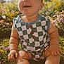 baby, infant, smiling, checkered_outfit, buttons, sitting, chubby_arms, legs, grass, flowers, outdoor, sunlight, portrait, closeup, happy, nature, garden, shoe, cute, skin