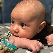 Elias is registered to the contest to win money with this photo: baby, infant, face, arm, pacifier, closeup, skin, hand, cushion, pattern, curious, lying_down, expression, indoors, child, young, cute, soft_light, portrait, baby_grooming