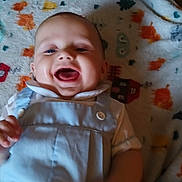 Waylon is registered to the contest to win money with this photo: baby, child, smiling, laughing, overalls, white_shirt, blanket, colorful, pattern, infant, happy, cute, face, mouth_open, indoor, clothing, person, skin, head, hand