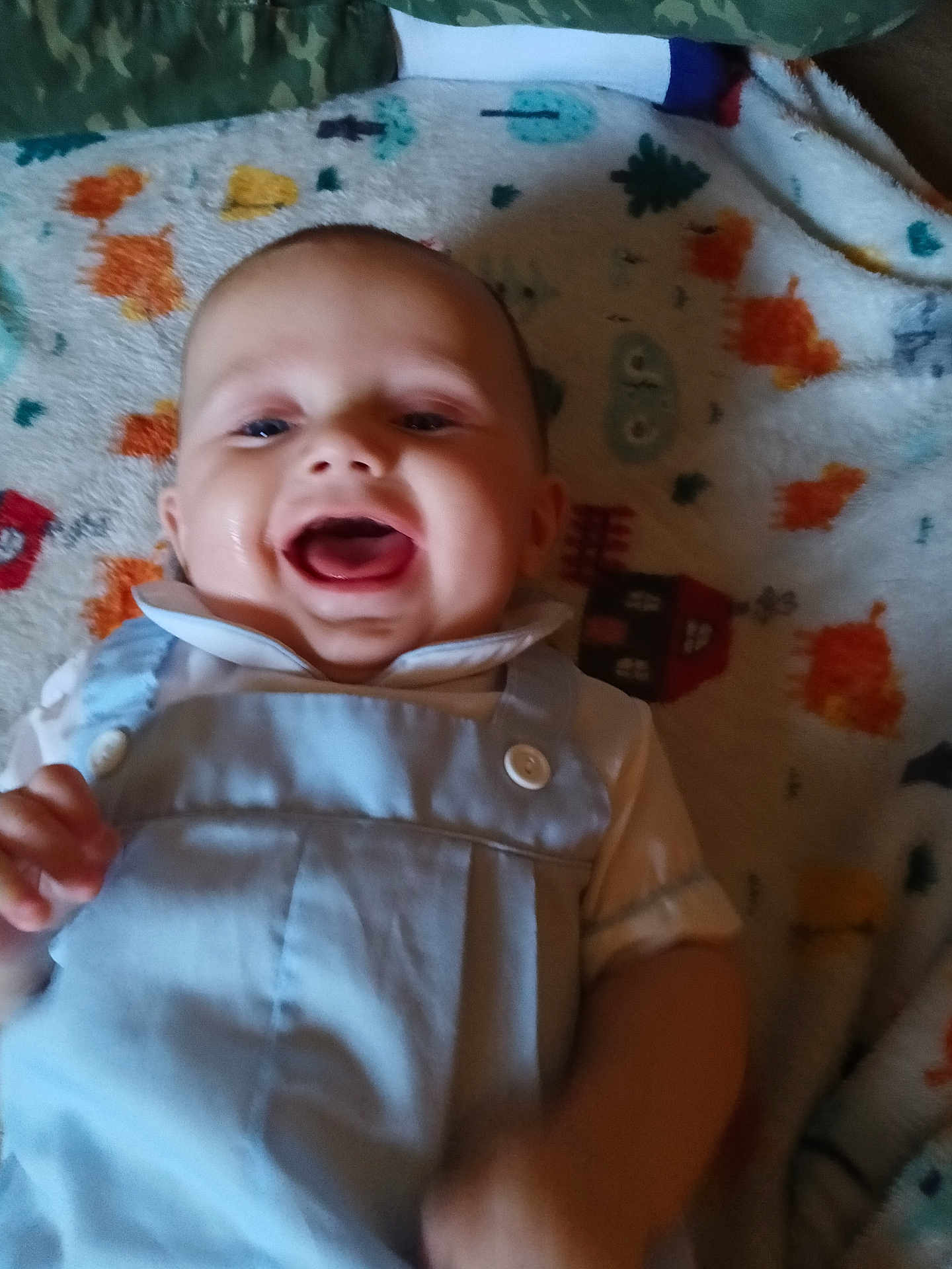 Waylon is registered to the contest to win money with this photo: baby, child, smiling, laughing, overalls, white_shirt, blanket, colorful, pattern, infant, happy, cute, face, mouth_open, indoor, clothing, person, skin, head, hand