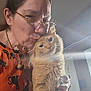 person, cat, orange_cat, glasses, indoor, affection, cuddling, sweater, long_hair, pet, love, cozy, closeup, fluffy_cat, hand, face, feline, domestic_animal, casual, home
