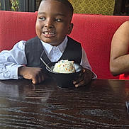 Joon Oakley is registered to the contest to win money with this photo: bowl, boy, child, decor, food, furniture, happy, ice_cream, indoor, lighting, patterned_wall, portrait, red_bench, restaurant, shirt, smile, spoon, table, vest, window