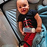 Derrell is registered to the contest to win money with this photo: baby, bottle, blanket, black_shirt, child, clothing, crib, face, furniture, happy, infant, indoors, person, playpen, pillow, red_pants, smile, toy, wearing, young_child
