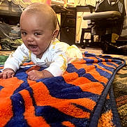 Derrell is registered to the contest to win money with this photo: baby, infant, child, blanket, orange, blue, tiger_stripe, carpet, indoor, furniture, chair, smiling, happy, crawling, floor, person, home, cute, cozy, playtime