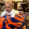 baby, infant, child, blanket, orange, blue, tiger_stripe, carpet, indoor, furniture, chair, smiling, happy, crawling, floor, person, home, cute, cozy, playtime