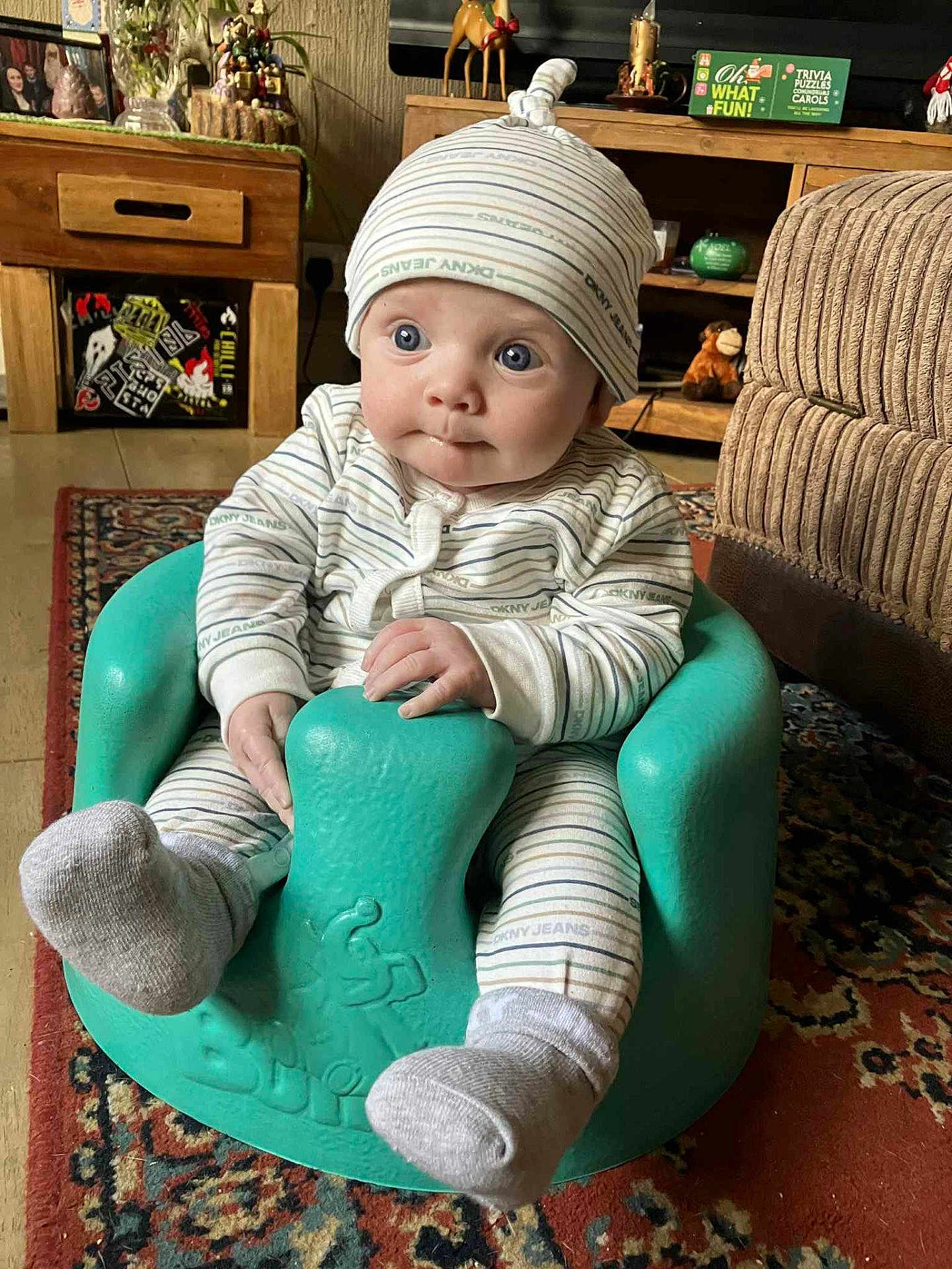 Caleb James joined the competition — help win amazing prizes! baby, infant, child, pajamas, hat, turquoise_seat, living_room, carpet, wooden_furniture, decorations, curious, sitting, cozy, hands, face, blue_eyes, sock, striped_clothing, indoors, portrait