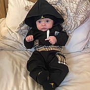 Caleb James joined the competition — help win amazing prizes! baby, bed, blanket, black_clothing, blue_eyes, child, cozy, face, fashion, hoodie, indoor, infant, looking, person, plaid_pattern, pillow, portrait, sitting, soft_texture, young_child