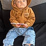 bear_ears, brown_hoodie, casual_clothing, child, couch, curious, cushion, flower, holding, home_decor, hoodie, indoor, jeans, person, portrait, serious_expression, socks, statue, table, toddler