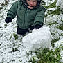 child, cold_weather, fence, gloves, grass, green_jacket, happy, hat, nature, outdoor, person, play, portrait, seasonal, smiling, snow, snowball, toddler, winter_clothing, young_child