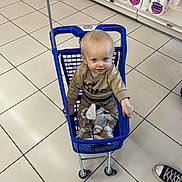 Raphaël participe au concours pour gagner de l'argent avec cette photo : aisle, baby, blue_cart, child, clothing, curious, cute, floor_tiles, indoor, person, pointing, retail, shoes, shopping, shopping_cart, store, supermarket, toddler, toilet_paper, toy