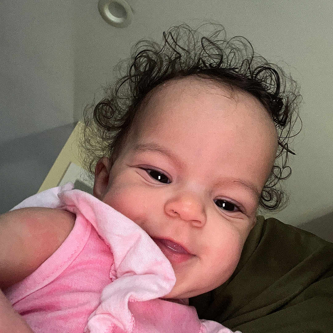 Sophia joined the competition — help win amazing prizes! baby, child, curly_hair, pink_clothing, smile, face, portrait, infant, cute, indoor, person, closeup, human, skin, young_child, happy, head, expression, holding, casual